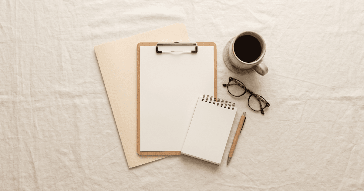 A flat-lay of organized paper records: a clipboard with a blank sheet, a manila folder, a notepad, and a ceramic mug, on a warm cream linen background.